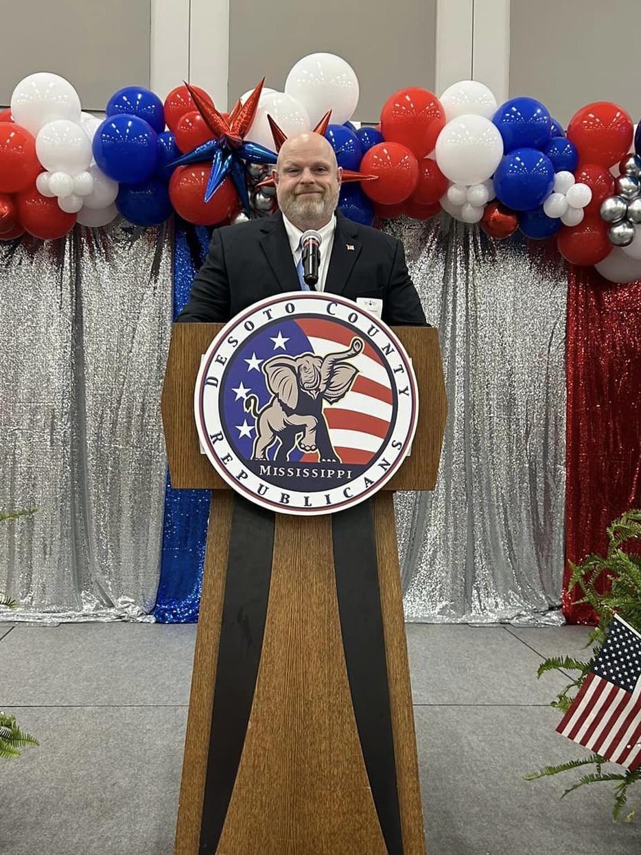 Jon Stevenson standing at a podium with balloons behind him